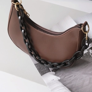 Detailed view of the brown crescent bag featuring matte leather and a thick black chain strap
