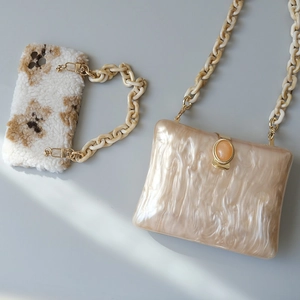 Close-up of champagne acrylic clutch with resin chain and orange gemstone clasp detail
