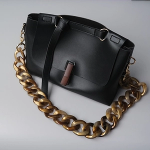 Detalle de bolso en cuero negro con cadena de resina ámbar y hebilla rectangular