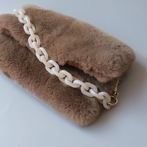 Detail of plush brown faux fur handbag with chunky white acrylic chain and gold metal hooks