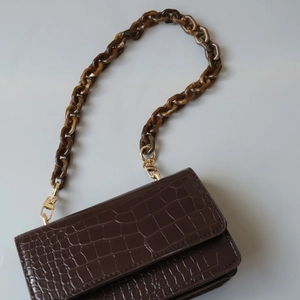 Detail of dark brown croc-embossed small crossbody bag with amber acrylic chain strap
