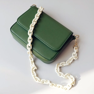 Detail of dark green leather shoulder bag with white acrylic chain and gold metal buckle