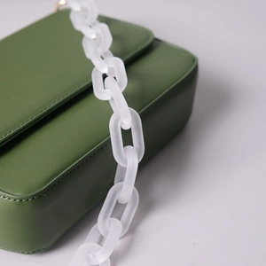 Close-up of matte white acrylic chain link attached to a vintage green leather handbag