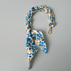 Détail de la chaîne de sac en métal doré entrelacée d'un foulard en soie à fleurs bleues