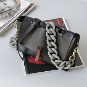 Detail of matte black leather bag featuring chunky grey resin chain and wood grain clasp