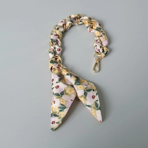 Gros plan de la bandoulière en chaîne dorée entrelacée de tissu floral et fermoir