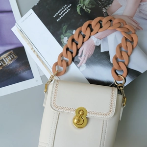 Detail of beige leather bag featuring orange resin chain and golden metal twist lock