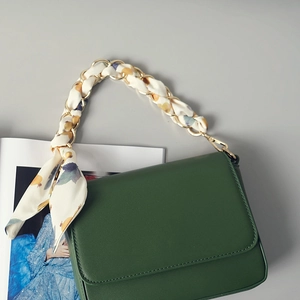 Détail d'une bandoulière en chaîne dorée entrelacée de soie sur un sac vert foncé