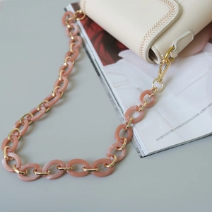 Détail de la chaîne en résine marbrée rose et maillons dorés sur un sac crème