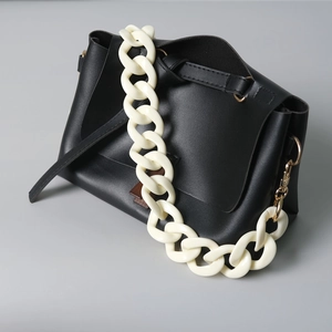 Detail of a black leather crossbody bag featuring a thick cream acrylic chain and gold hardware