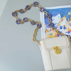 Detail of cream crossbody bag with chunky purple acrylic and gold chain strap