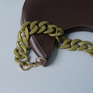 Detail of olive green acrylic chain strap with gold metal clasp on brown leather bag