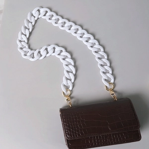 Detail view of brown crocodile texture bag with white acrylic chain and gold hooks