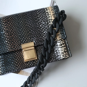 Detail of snake skin texture purse with golden lock and matte black resin chain