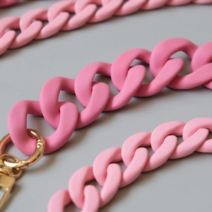 Macro view of matte pink acrylic chain links with gold lobster clasp for handbags