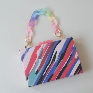 Macro shot of rectangular acrylic clutch featuring colorful abstract stripes and rainbow chain