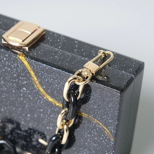 Dettaglio pochette in acrilico nero glitterato con chiusura e catena dorata lucida