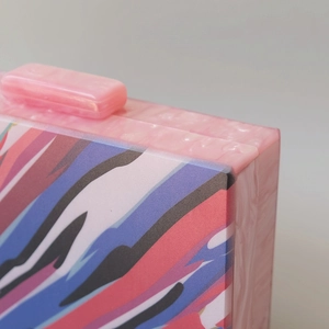 Detail of the acrylic clutch bag showing the pink marble texture and colorful stripe pattern