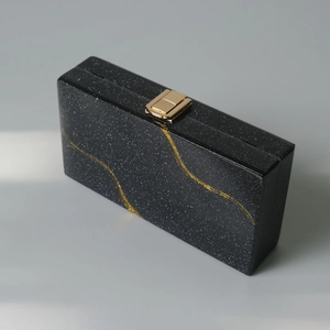 Dettaglio della pochette in acrilico glitter nero con venature dorate e chiusura in metallo