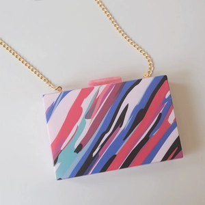 Close-up of artistic acrylic evening bag with colorful stripes and gold chain strap