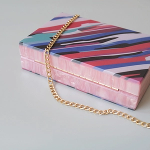 Detail of colorful geometric striped acrylic clutch bag with marble finish and gold chain