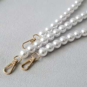Close-up of elegant white faux pearl bag straps with light gold lobster clasps detail