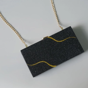 Dettaglio borsa da sera in acrilico nero con glitter e motivi curvi in oro lucido