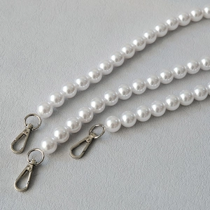 Close-up of white pearl bag straps with polished silver lobster clasps on grey leather