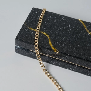 Dettaglio pochette da sera glitter nera con linee dorate fluide e tracolla a catena