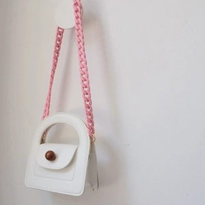 Close-up of a white mini handbag with a pink matte resin chain and brown ball clasp detail