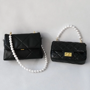 Detail of elegant pearl chain straps on quilted black leather handbags with gold clasps