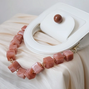 Close-up of white leather handbag featuring a marble resin block chain and round handle