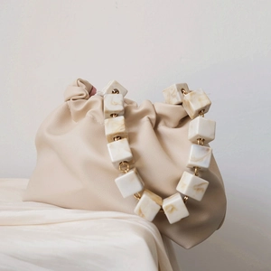 Detail of elegant beige gathered pouch bag with marble texture resin chain strap