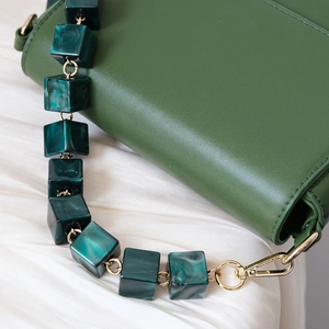 Detailed close-up of dark green leather bag with marbled resin cube chain and gold metal hooks