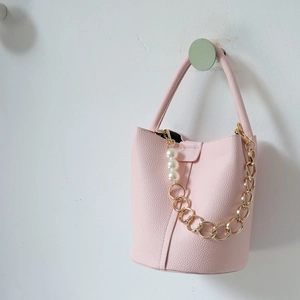 Pink lychee grain leather bucket bag featuring gold metal chain and large white pearls