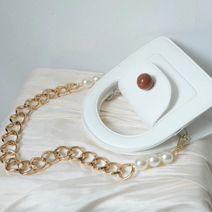Close-up of white leather handbag with golden chain and large decorative white pearls
