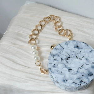 Detail of round marble acrylic handbag with gold chain and large white pearls decoration