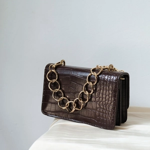 Detailed close-up of dark brown crocodile pattern leather bag with thick gold chain handle