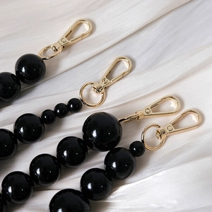 Detailed view of polished black resin beads on handbag chain with gold lobster clasp