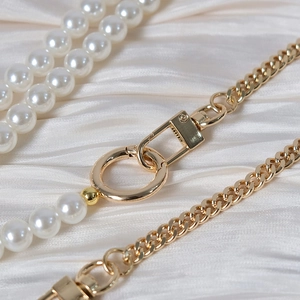 Close-up of white pearl and gold metal curb chain strap with lobster clasp on satin