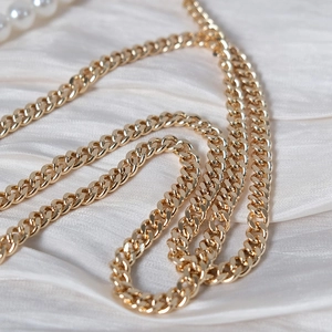 Macro shot of polished gold curb chain strap on a white silk background with pearls