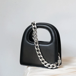 Detail of a black minimalist handbag with a chunky silver chain on silk fabric