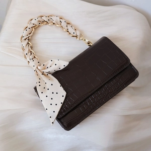 Detail einer braunen Kroko-Handtasche mit Goldkette und gepunktetem Seidenschal-Dekor