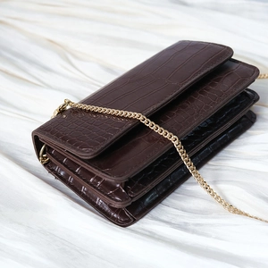 Detail of dark brown croc-pattern leather bag with gold chain on white silk