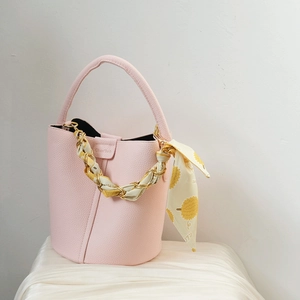 Detail of a pink bucket bag featuring a silk scarf wrapped metal chain handle accessory