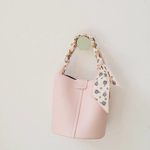 Detailed view of pink bucket bag featuring golden chain strap wrapped in floral silk scarf
