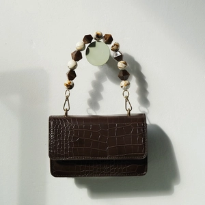 Macro detail of dark brown croc-pattern leather bag with marble resin bead handle