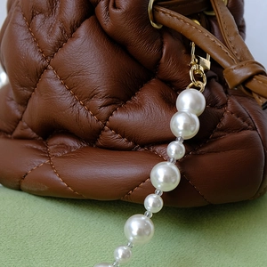 Détail d'un sac seau en cuir matelassé marron avec chaîne de perles blanches et boucle dorée
