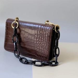 Detail of croco-embossed brown leather bag with marble acrylic chain and gold rings