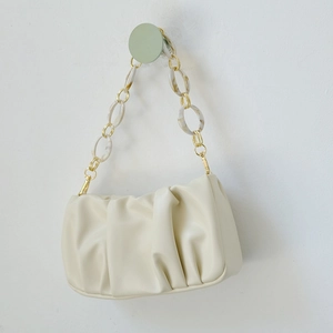 Chic beige pleated cloud bag with marble acrylic and gold chain strap hanging on hook